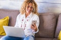 Freelance people at work at home - beautiful adult caucasian woman sit on the sofa with phone device and laptop computer working - Royalty Free Stock Photo
