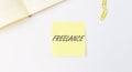 Freelance word on yellow paper on white table, top view