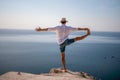 A digital nomad, a man in a hat, a businessman does yoga on the rocks by the sea at sunset time, does a business