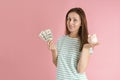 A freelancer girl in casual clothes smiles and holds hundred dollar bills and a piggy bank in her hands standing on a pink Royalty Free Stock Photo