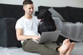 Freelancer guy with laptop and dog is working at home in quarantine to coronavirus infection