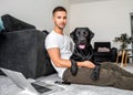 freelancer guy sitting at home working with a dog in an embrace, black labrador. Royalty Free Stock Photo