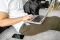 freelancer guy sitting at home working with a dog in an embrace, black labrador. Royalty Free Stock Photo