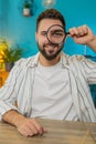 Freelancer man holds magnifying glass near face looking at camera with big zoomed eye, analyzing Royalty Free Stock Photo