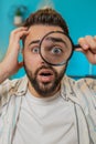 Freelancer man holds magnifying glass near face looking at camera with big zoomed eye, analyzing Royalty Free Stock Photo