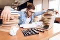 Freelancer man looking at notes frustrated at laptop sitting at desk surrounded by books. Royalty Free Stock Photo