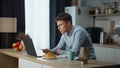 Freelancer man satisfied work sitting at kitchen table with modern laptop.