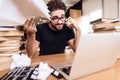 Freelancer man frustrated with notes at laptop sitting at desk surrounded by books. Royalty Free Stock Photo