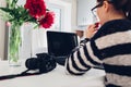 Freelancer photographer working in morning kitchen. Woman works on laptop using camera and pen tablet.