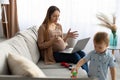 Freelancer pregnant mother working on laptop remotely from home, having video call, child boy playing near mom Royalty Free Stock Photo