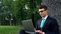 Freelancer sitting under tree in park and using laptop, remote work outdoors Royalty Free Stock Photo