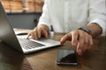 Freelancer taking smartphone while working on laptop at table indoors, closeup