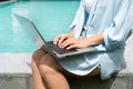 Freelancer using laptop working remotely near swimming pool. Young Asian traveler woman working on computer during her summer Royalty Free Stock Photo