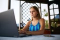 Freelancer woman sitting at garden house in tropical summer location and working with laptop remotely in swimsuit