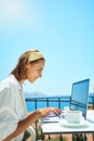 Freelancer woman using laptop computer browsing online, in wireless earphones at terrace