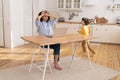 Freelance worker woman tired of noisy son work on laptop computer in kitchen with small son running