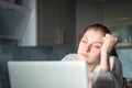 Freelancer yawns. Young woman sitting in the kitchen at home looks tired and yawning while working at a laptop. Business