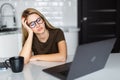 Freelancer yawns. Young sleepy woman sitting in the kitchen at home looks tired and yawning while working at a laptop. Business in