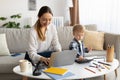 Freelancing at maternity leave. Young mother working on laptop while her toddler son playing with calculator neaby Royalty Free Stock Photo