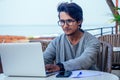 Freelancing and remote work.handsome male student working laptop keyboard sitting in cafe on the beach with free Royalty Free Stock Photo