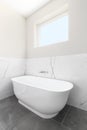 A freestanding bathtub on a grey tiled floor.