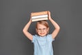 Freestyle. Little girl in eyeglasses isolated on grey with books above the head smiling kind Royalty Free Stock Photo