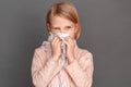 Freestyle. Little girl in scarf isolated on grey blowing nose into tissue looking aside concerned close-up Royalty Free Stock Photo