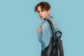 Freestyle. Man in denim shirt with backpack standing isolated on gray looking back close-up