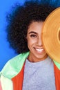 Freestyle. Mulatto girl standing isolated on blue covering eye with phonograph record laughing playful close-up