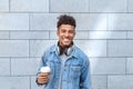 Freestyle. Mulatto guy with headphones on neck standing isolated on wall with cup of coffee smiling toothy