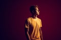 Freestyle. Mulatto guy standing isolated on dark red in yellow light looking aside pensive