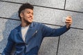 Freestyle. Mulatto guy standing on wall taking selfie on smartphone smiling toothy side view