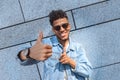 Freestyle. Mulatto guy in sunglasses standing isolated on wall showing thumb up smiling cheerful close-up