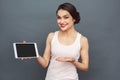 Freestyle. Woman standing isolated on grey showing screen of digital tablet smiling playful