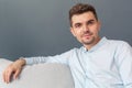 Freestyle. Young man studio sitting on sofa on grey smiling calm close-up