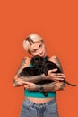 Freestyle. Young tattoed woman standing isolated on orange holding cute puppies hugging tender