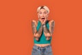 Freestyle. Young tattoed woman standing isolated on orange holding faec screaming shocked