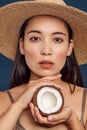 Freestyle. Young woman in hat standing isolated on dark blue holding coconut thoughtful close-up