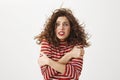 It is freezing cold outside. Indoor shot of poor attractive girl with curly hair that flows on wind, hugging herself and Royalty Free Stock Photo