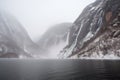 freezing fiord with view of towering waterfall, surrounded by mist