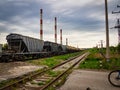 Freight cars of the train pass against the background of the pipes of the factory sky with clouds of green grass. Royalty Free Stock Photo