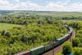 The freight railroad train rides through fields and hills amidst green meadows and trees Royalty Free Stock Photo
