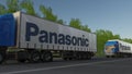 Freight semi trucks with Panasonic Corporation logo driving along forest road. Editorial 3D rendering