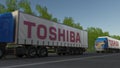 Freight semi trucks with Toshiba Corporation logo driving along forest road. Editorial 3D rendering