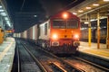 Freight train arrives at the station during nighttime with cargo containers illuminated by platform lights Royalty Free Stock Photo