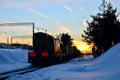 Freight train with cars on the railway leaves the depot against the backdrop of an incredible sunset in the winter period.