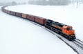 Freight train moves on railway through snowy fields. Cargo containers travel on tracks in winter landscape. Engine pulls wagons Royalty Free Stock Photo