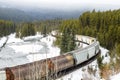 Freight train running alongside a frozen river in a forested mountain landscape Royalty Free Stock Photo