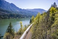 Freight train travels by rail along the Columbia River with a ridge of mountains on the opposite bank of the Columbia Gorge Royalty Free Stock Photo
