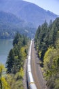Freight wagon train travels by rail road along the Columbia River with high forest mountains at Columbia Gorge Royalty Free Stock Photo